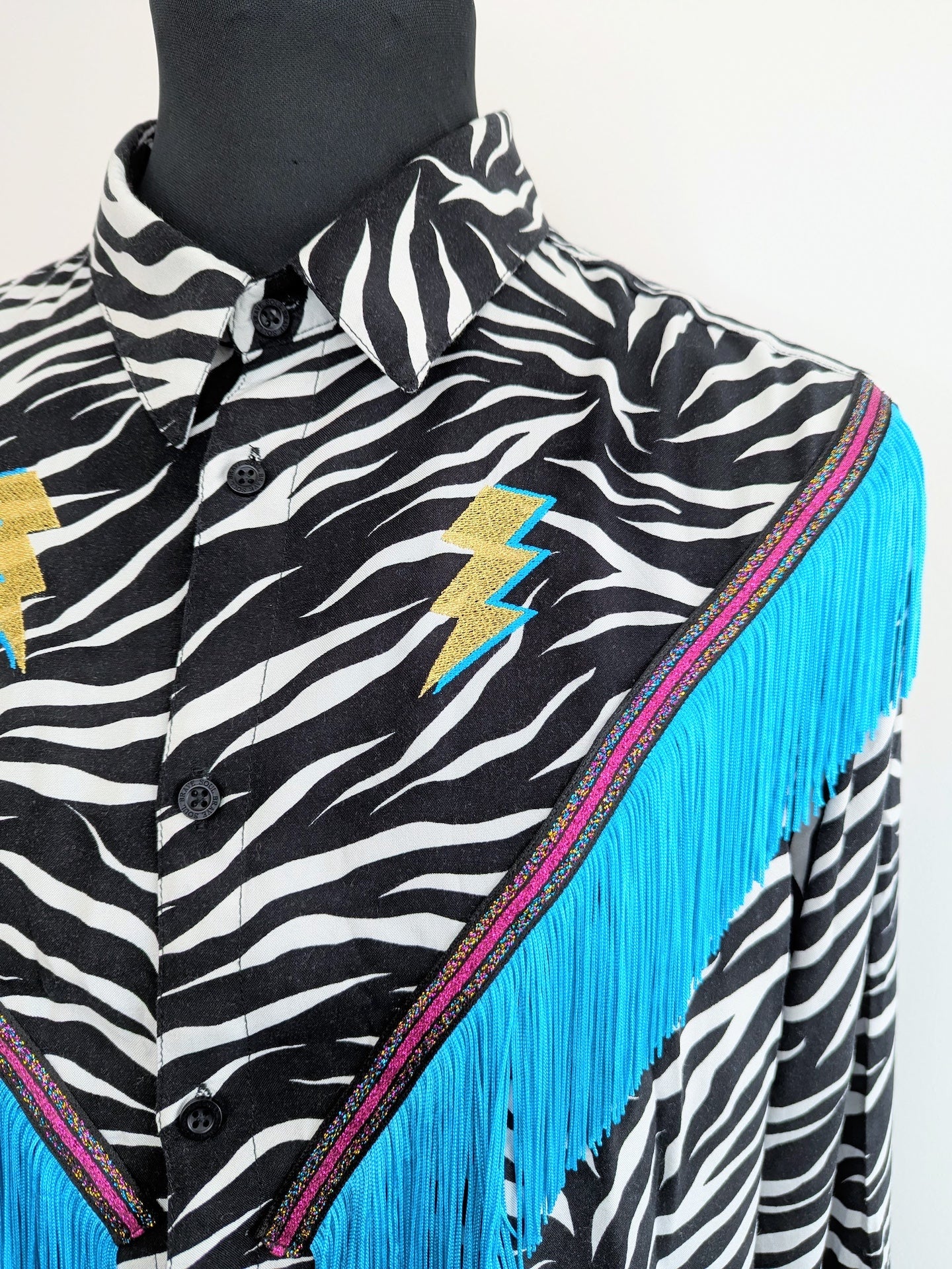 rodeo style western fringe shirt with embroidered  gold lighting bolts and turquoise tassel trim 