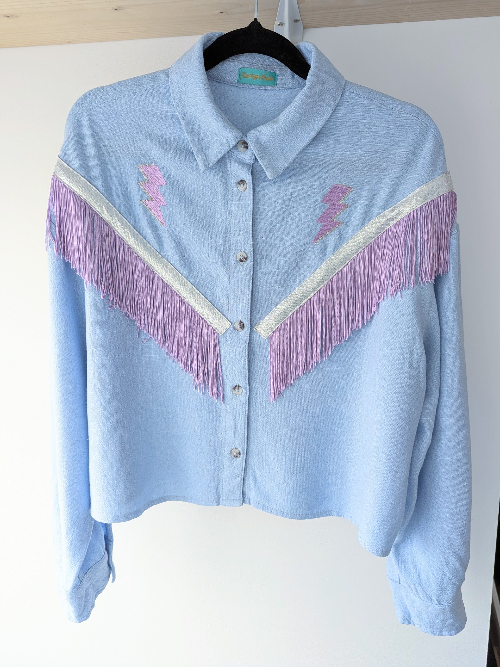 Light blue shirt with purple fringe trim and lightning bolt designs on a white background