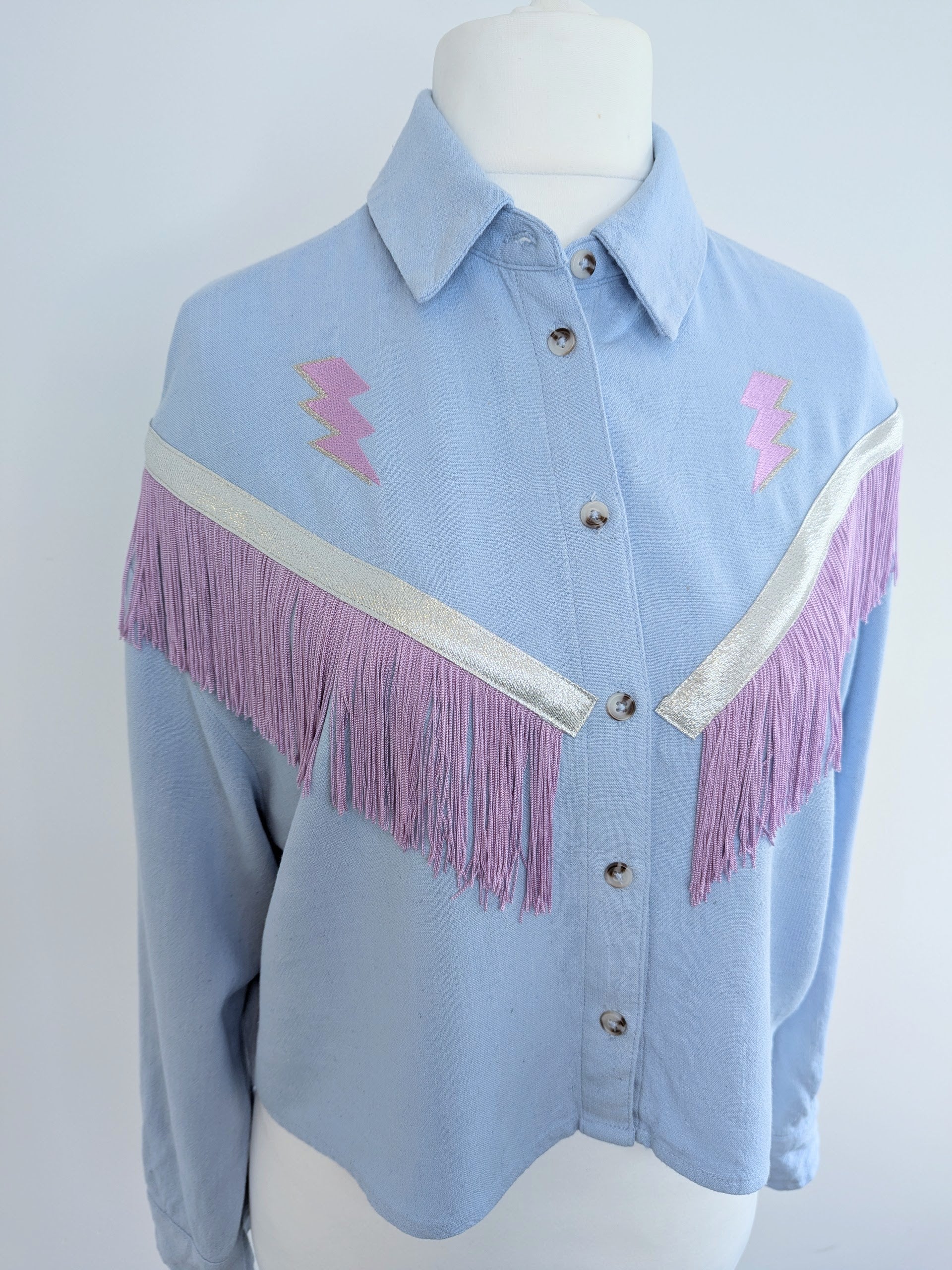 Light blue shirt with lilac western style fringe accents on a mannequin against a white background