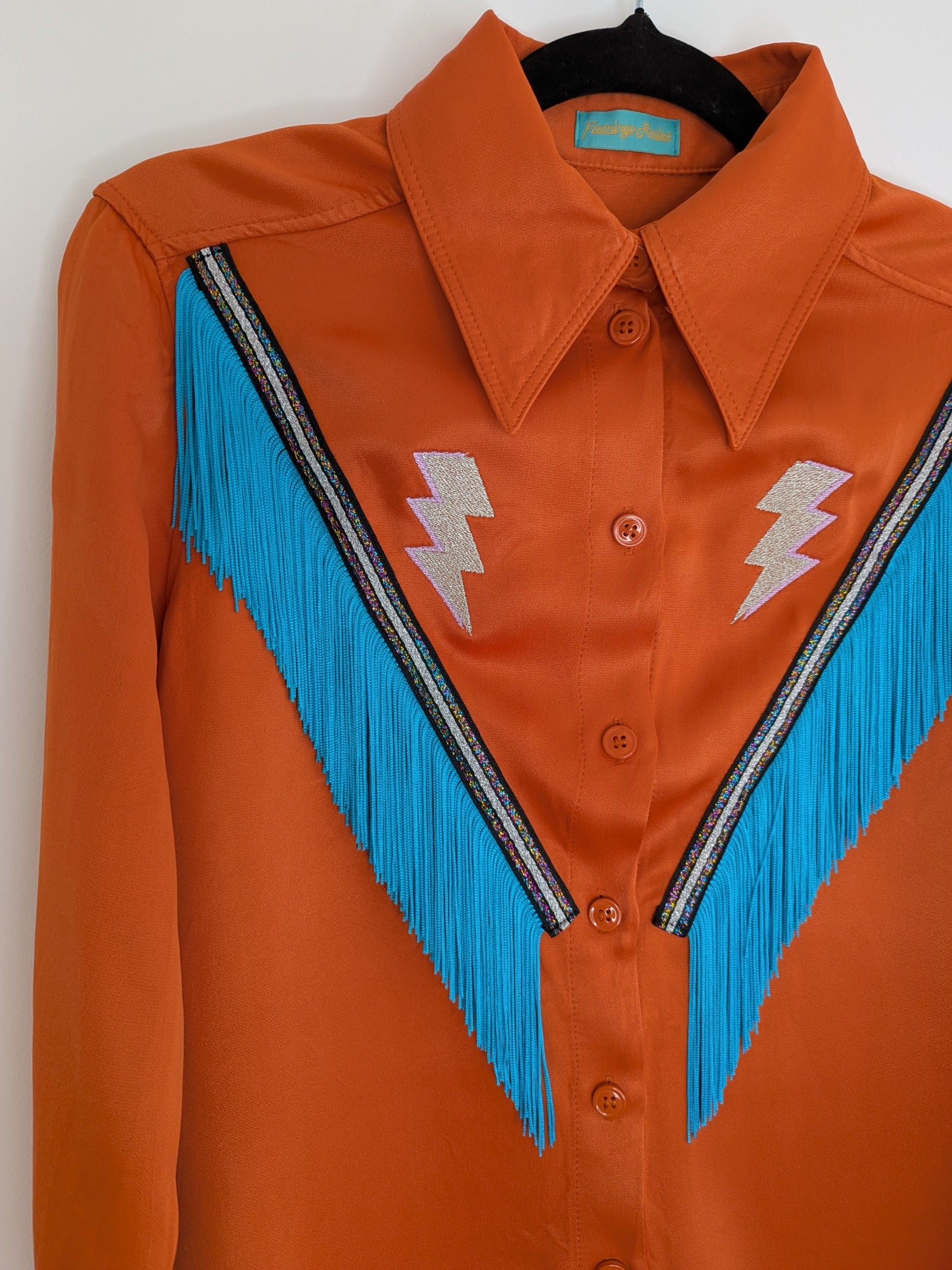 Orange satin shirt with blue fringe trim and lightning bolt designs on a white background