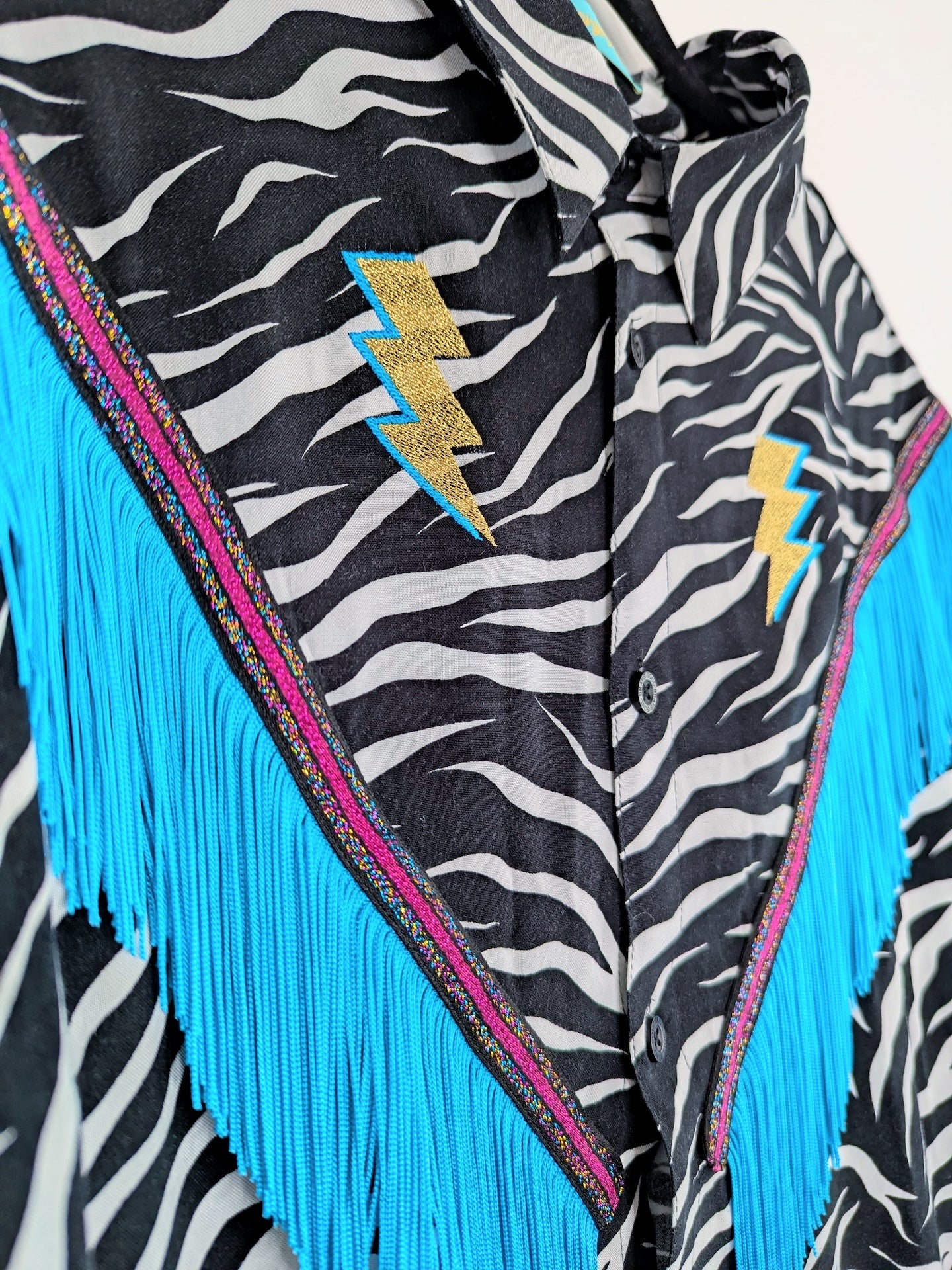 Zebra print button up with blue fringes and lightning bolt designs on a white background