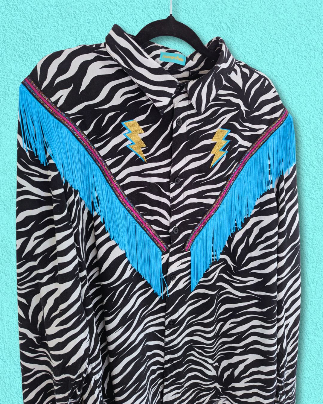 Zebra print jacket with turquoise fringe and lightning bolt designs on a turquoise wall background