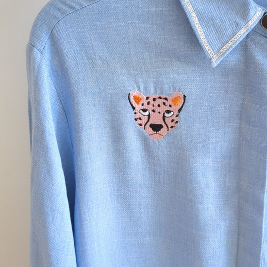 Light blue shirt with embroidered cheetah faces on a beige background 