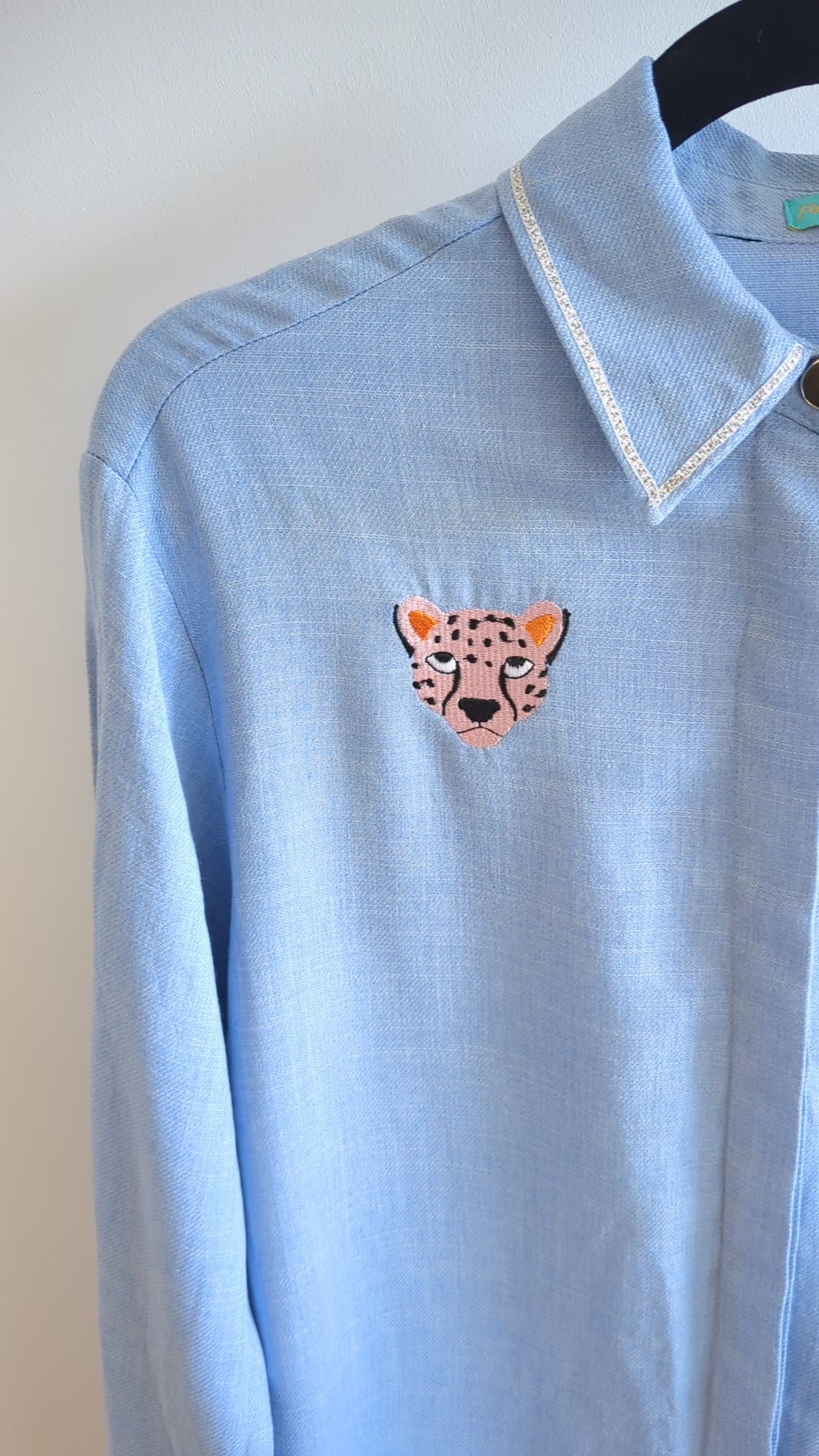 Light blue shirt with embroidered cheetah faces on a beige background 