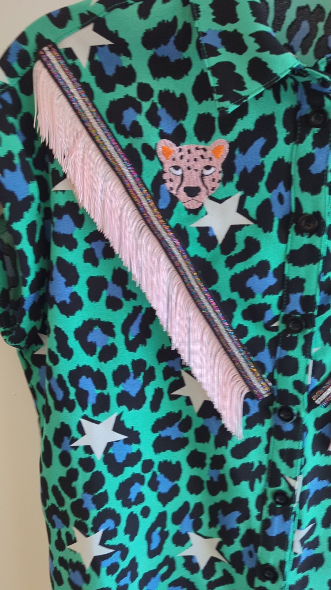 video of a green shirt with leopard print and star patterns. It has embroidery pink leopards and western style pale pink fringe trim added.
