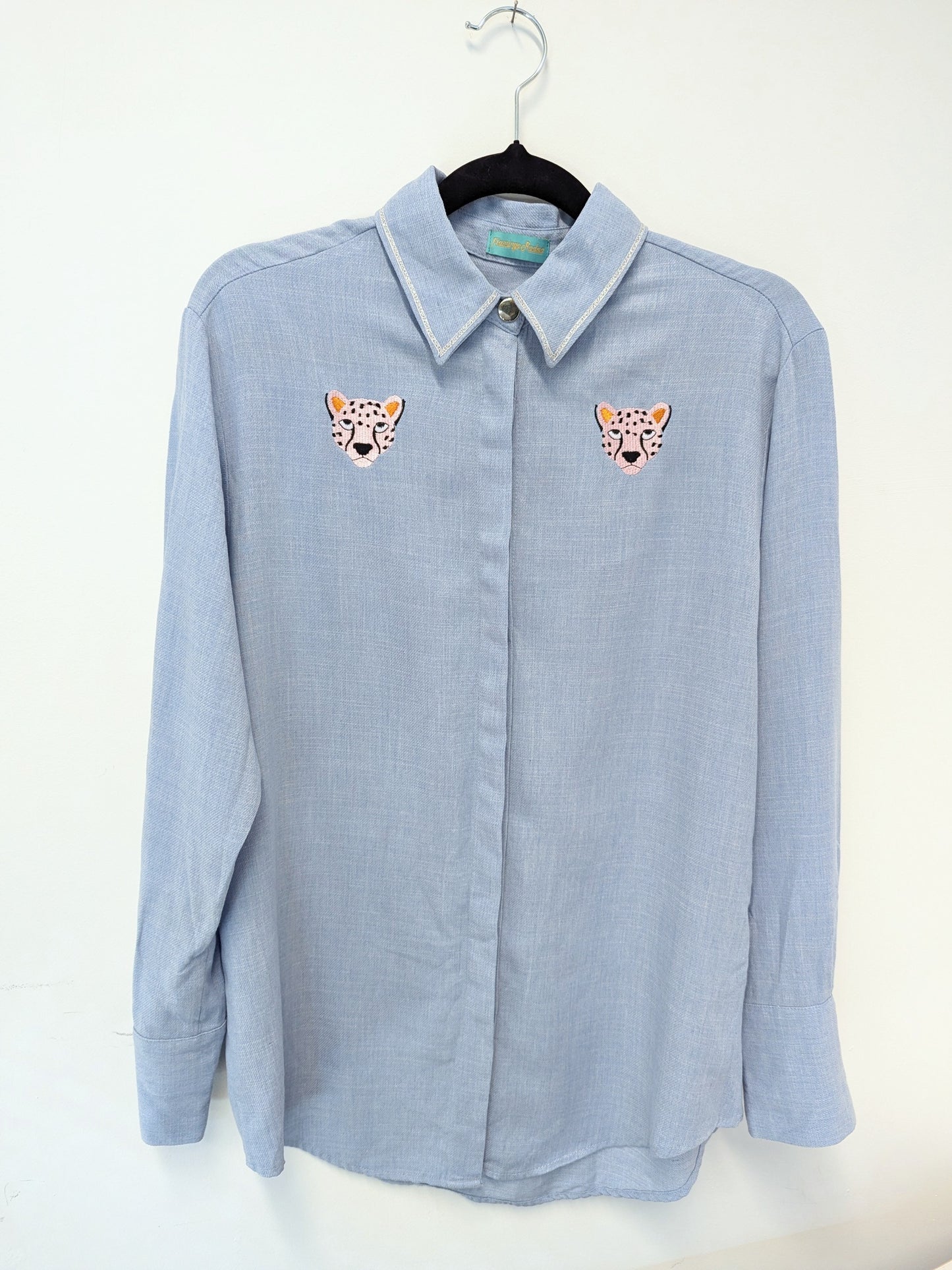 Light blue shirt with contrast silver ribbon trim on the collar and embroidered cheetah faces on a beige background