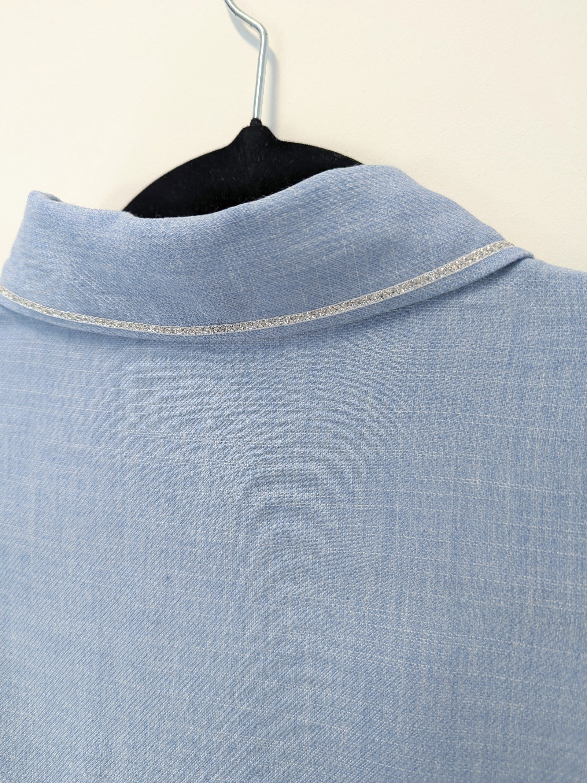 Close-up of a light blue shirt with a silver trim collar on a hanger against a white background