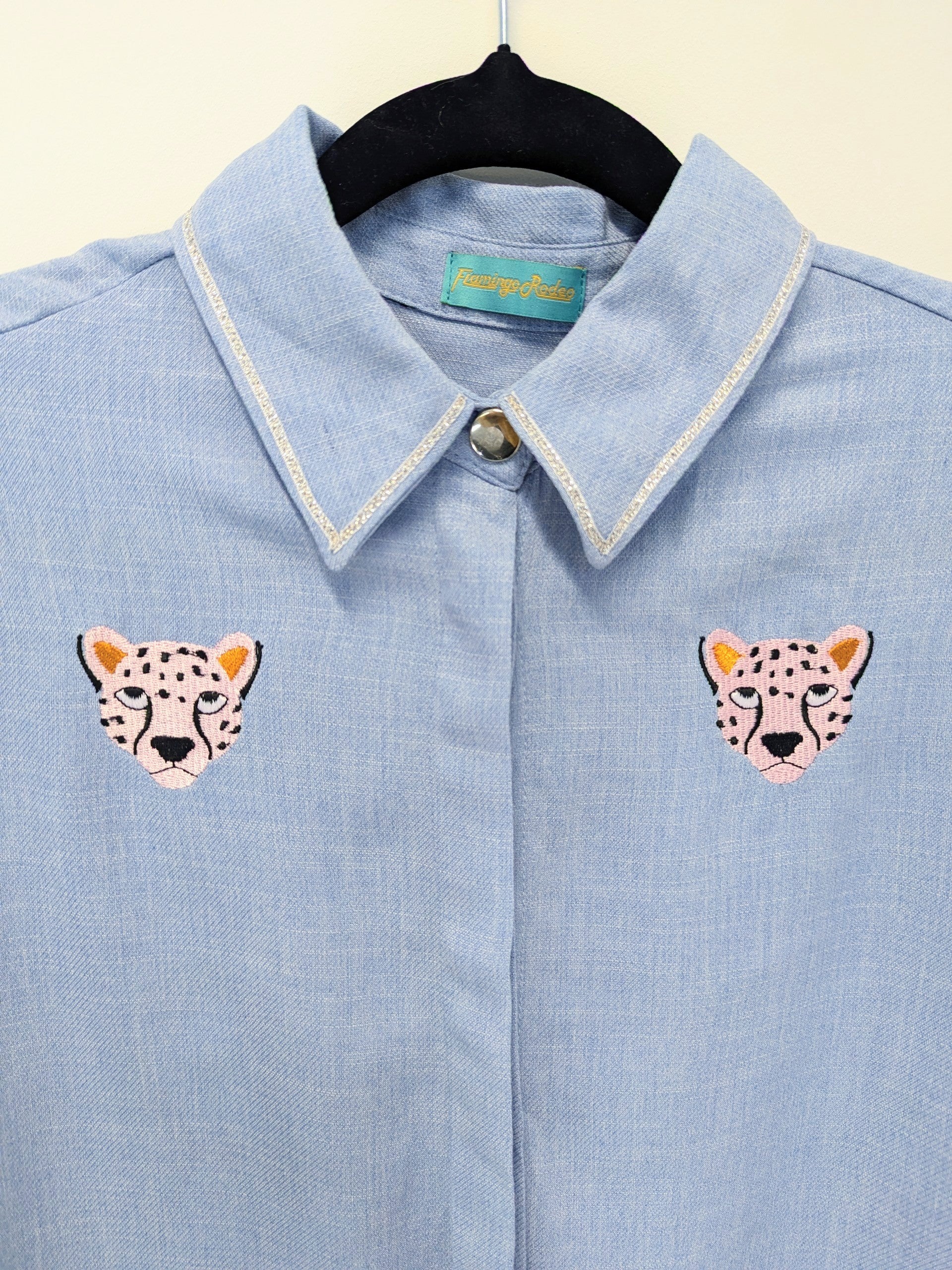 Light blue shirt with embroidered cheetah faces on a beige background