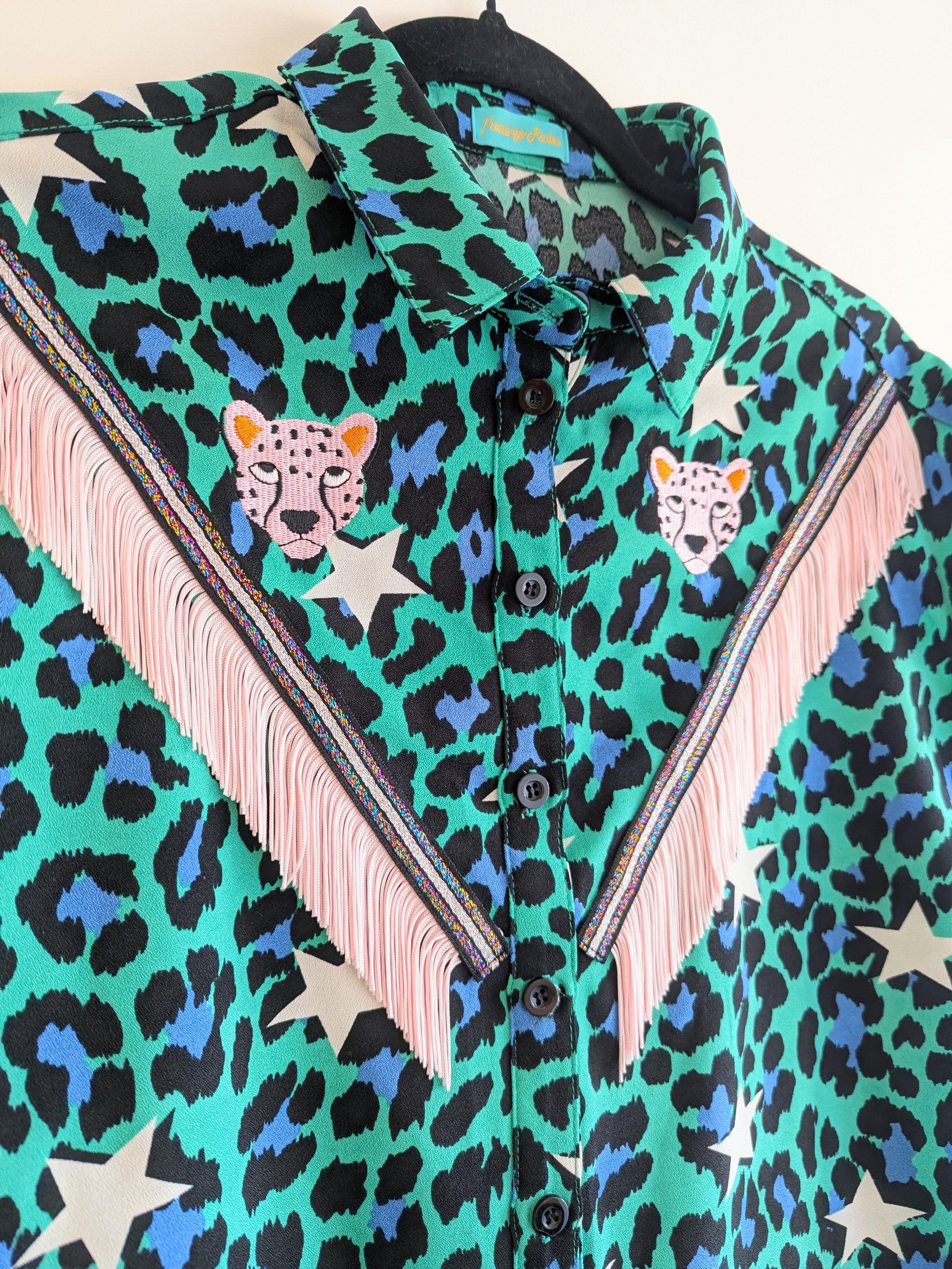 green shirt with leopard print and star patterns. It has embroidery pink leopards and western style pale pink fringe trim added.