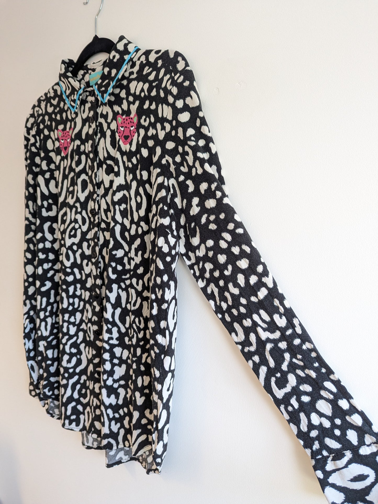 Long sleeve black and white animal print shirt with embroidery pink leopard faces on a white background. The shirt has a contrast teal ribbon on the collar. 