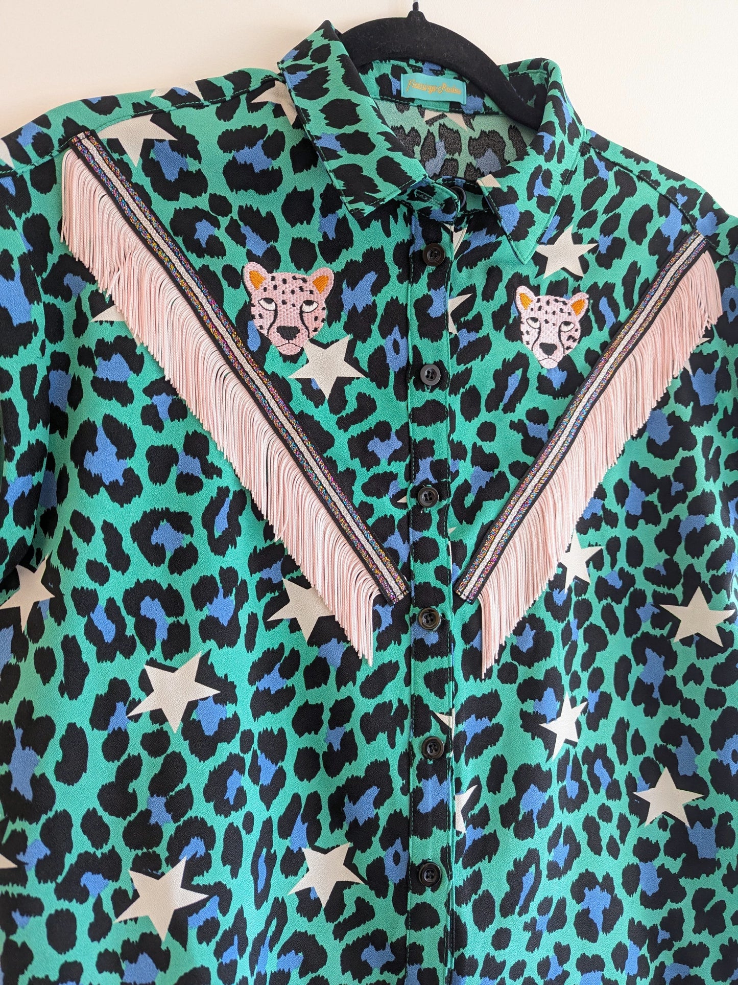 green shirt with leopard print and star patterns. It has embroidery pink leopards and western style pale pink fringe trim added.