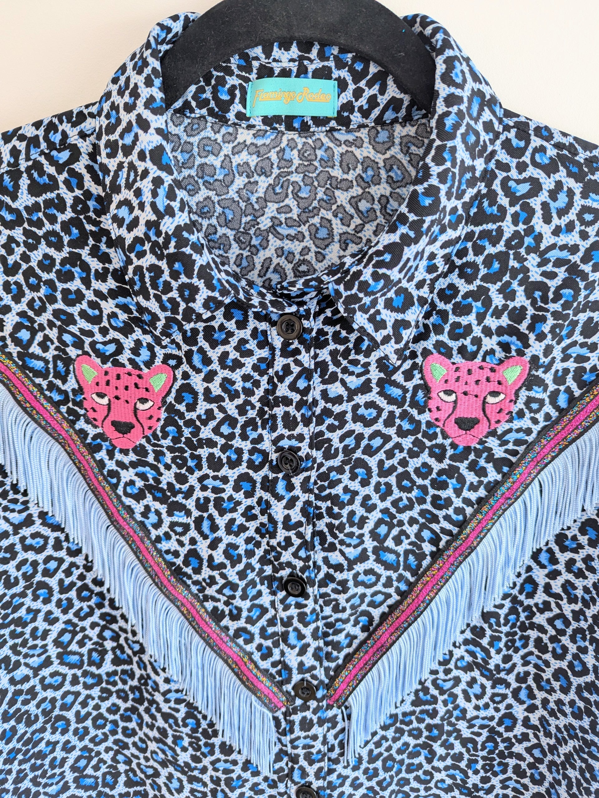 blue leopard print shirt with embroidery pink leopard faces above a v shape of cowboy western style fringe trim