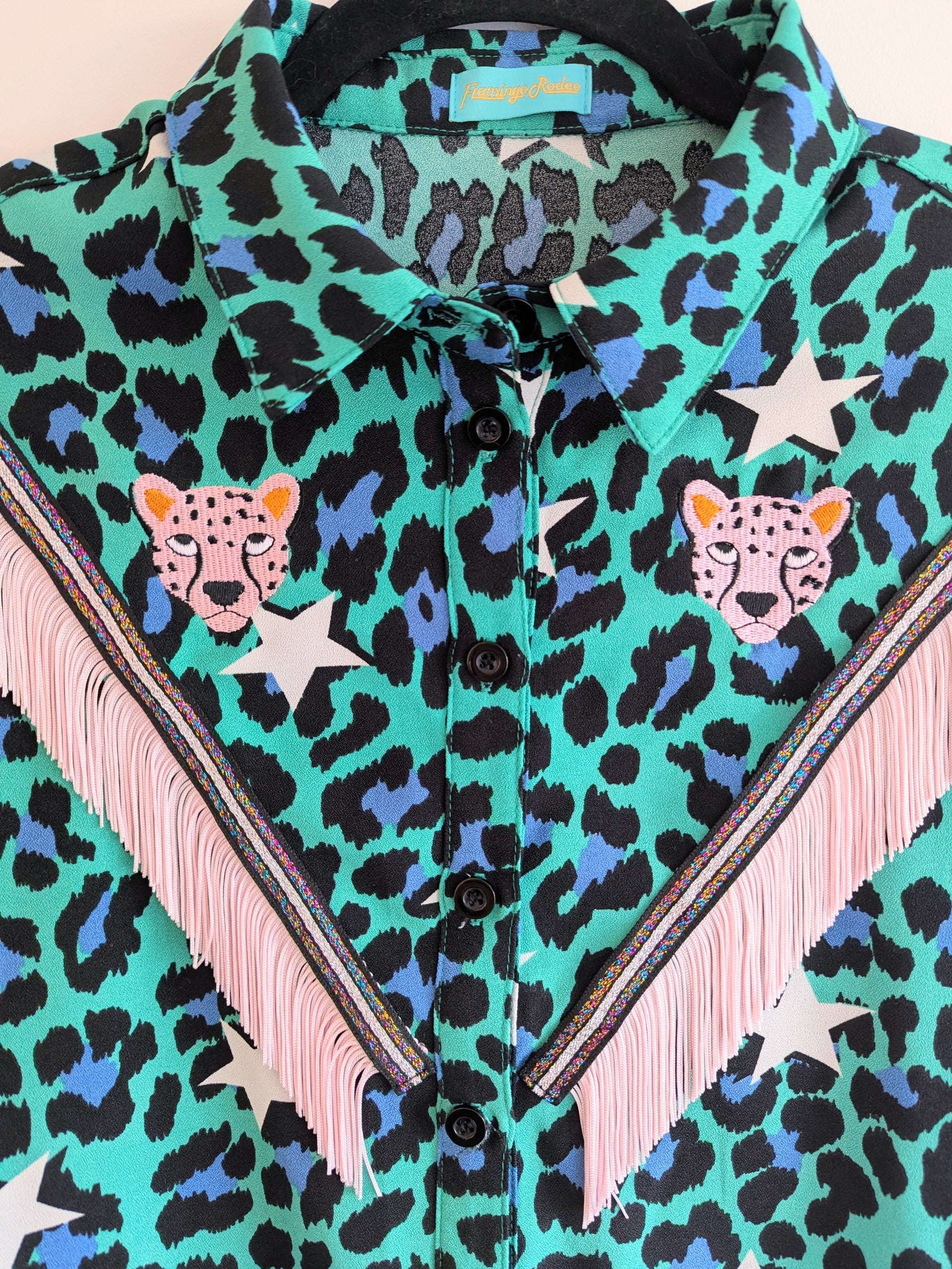 green shirt with leopard print and star patterns. It has embroidery pink leopards and western style pale pink fringe trim added.