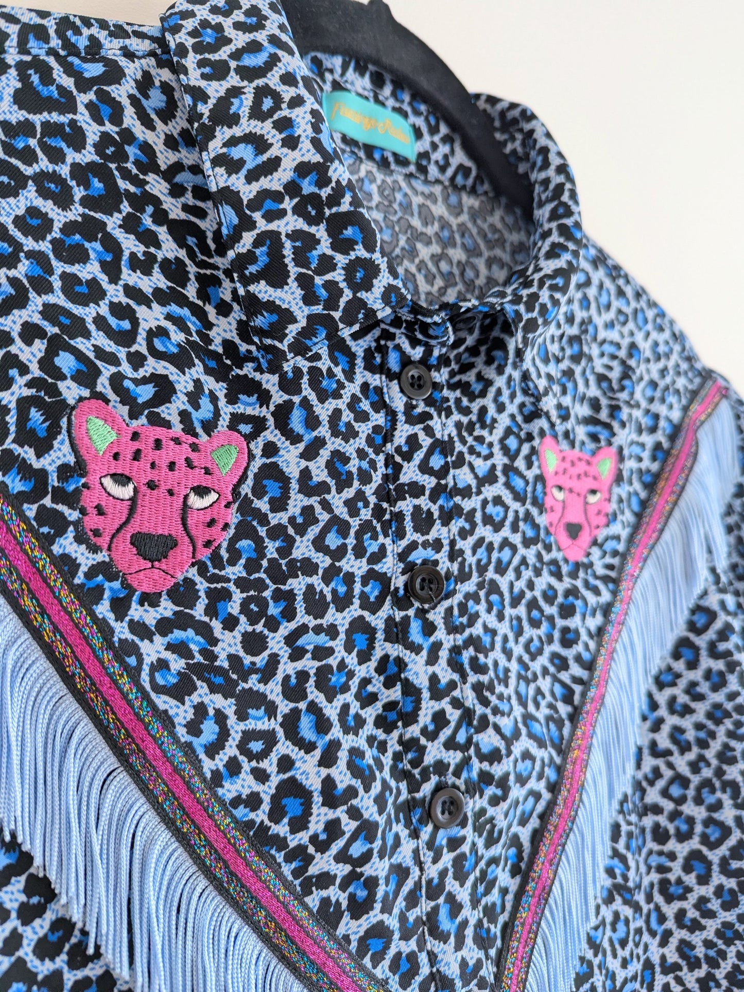 blue leopard print shirt with embroidery pink leopard faces above a v shape of cowboy western style fringe trim
