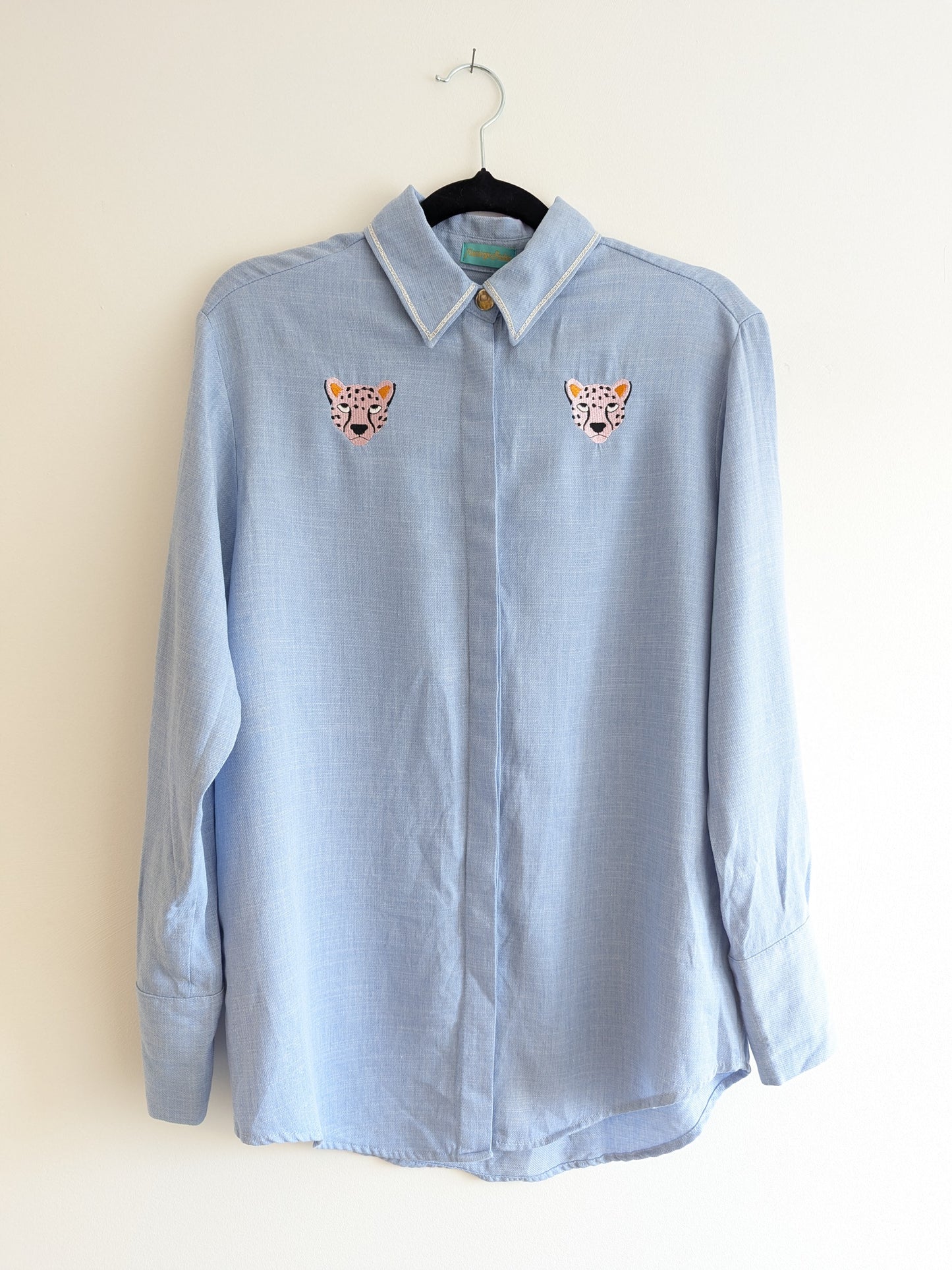 Light blue shirt with embroidered cheetah faces on a beige background
