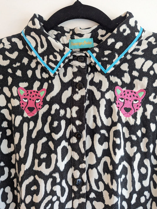 Black and white animal print shirt with embroidery pink leopard faces on a white background. The shirt has a contrast teal ribbon on the collar. 
