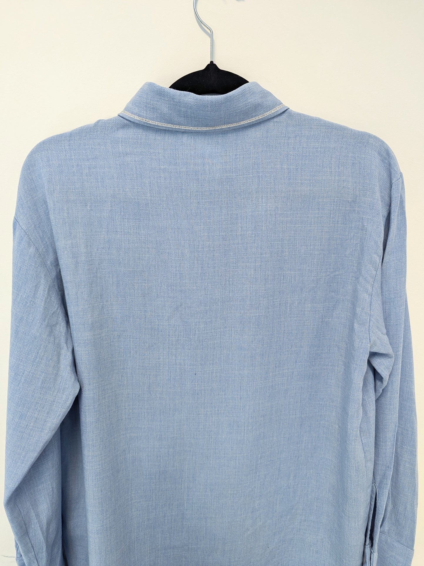 Close-up of a light blue shirt with a silver trim collar on a hanger against a white background